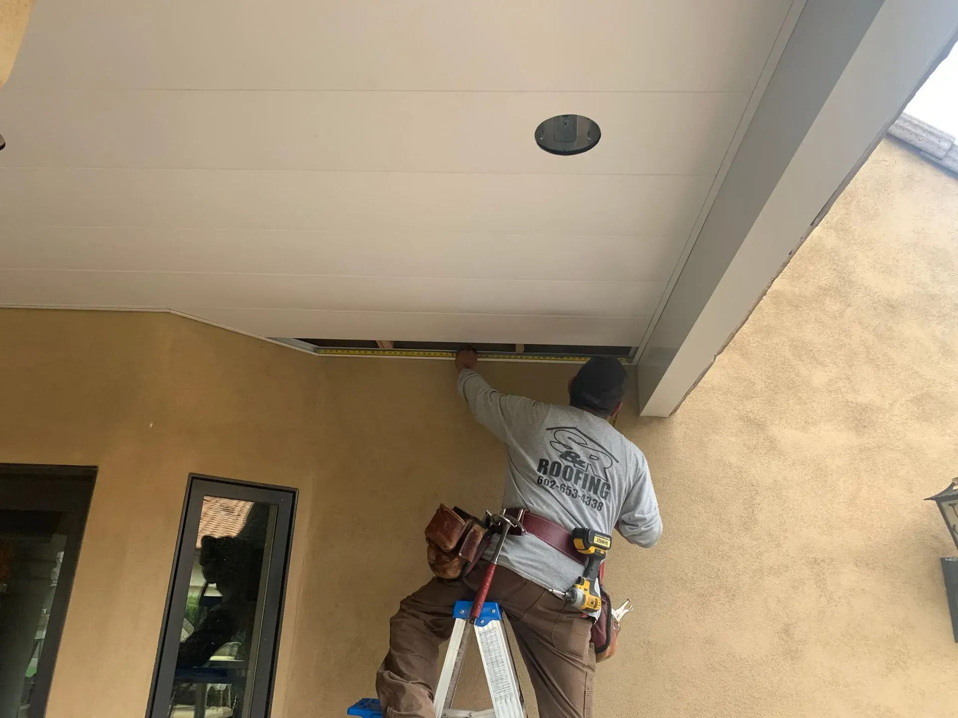 Worker on a ladder fixing a recessed ceiling light under a covered patio