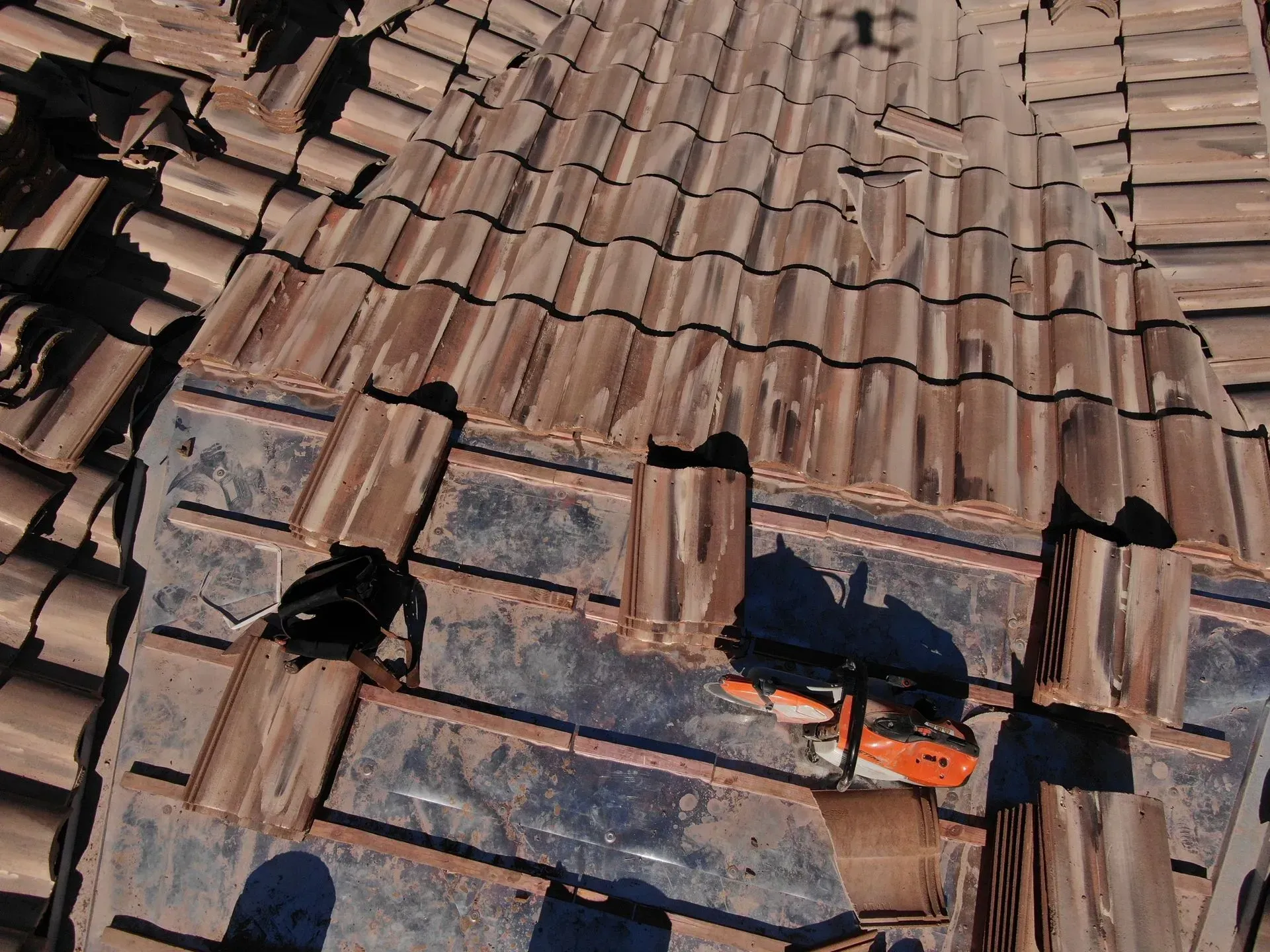 Damaged terracotta roof tiles with a small black cat lying near the lower right corner