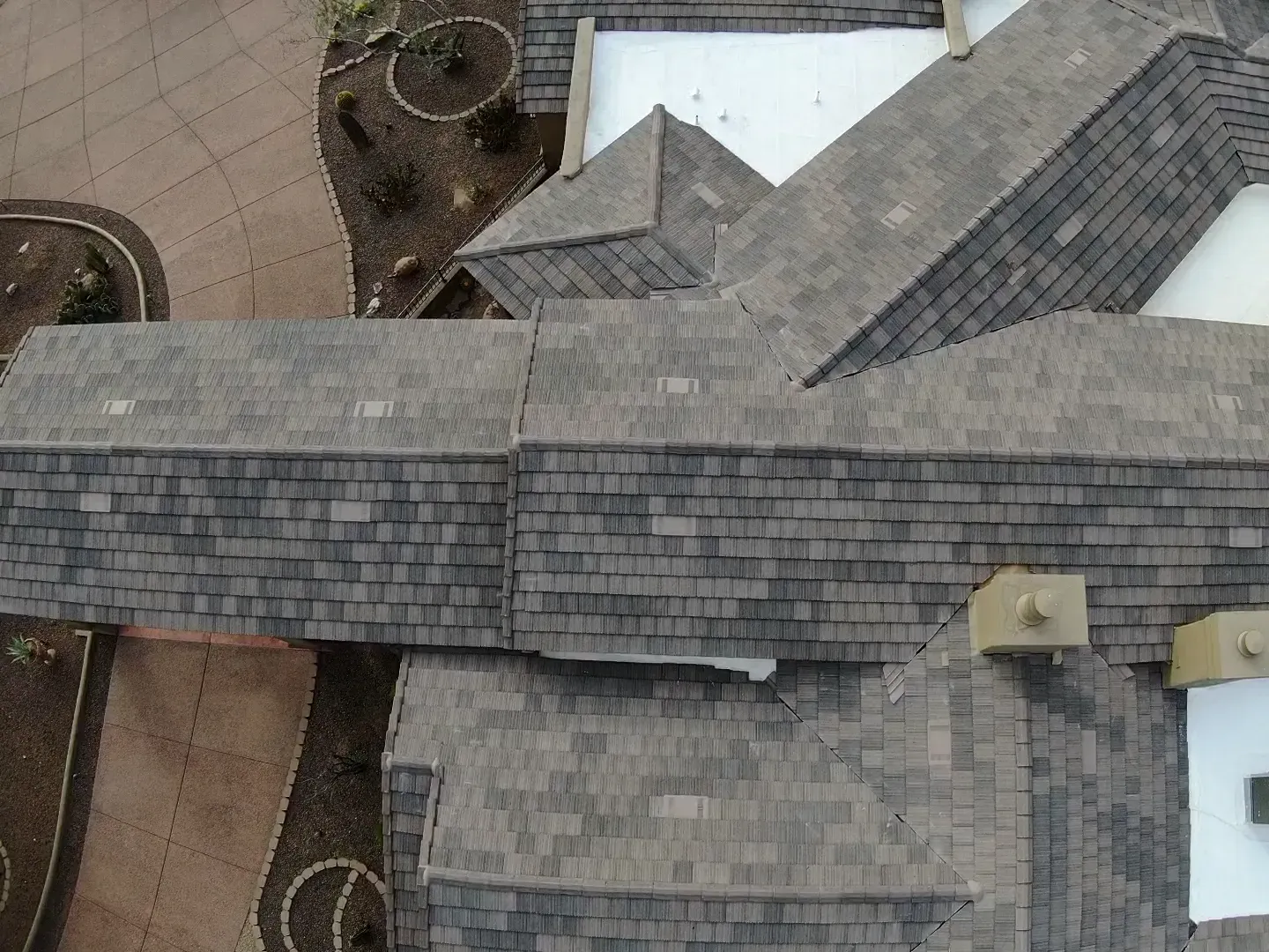 Aerial view of a shingled rooftop with intersecting sections and a patio area beside it.
