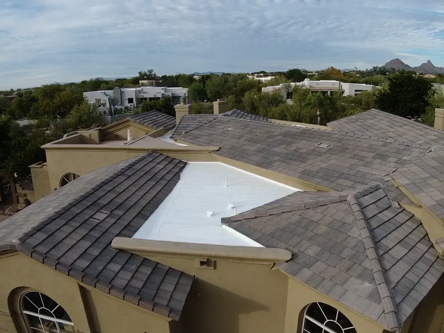 Rooftop with gray shingles and a white tarp patch, viewed over nearby homes and trees