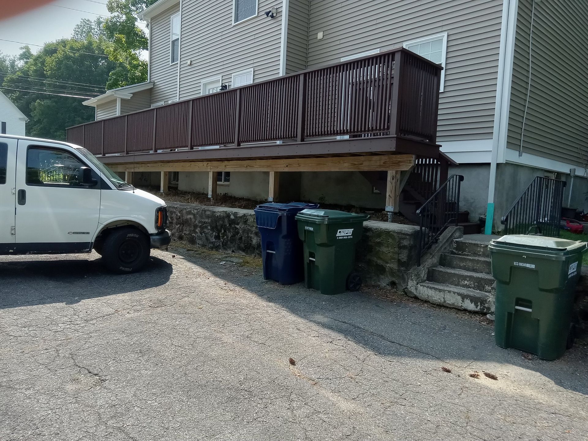 A white van is parked in front of a house with a deck and trash cans.