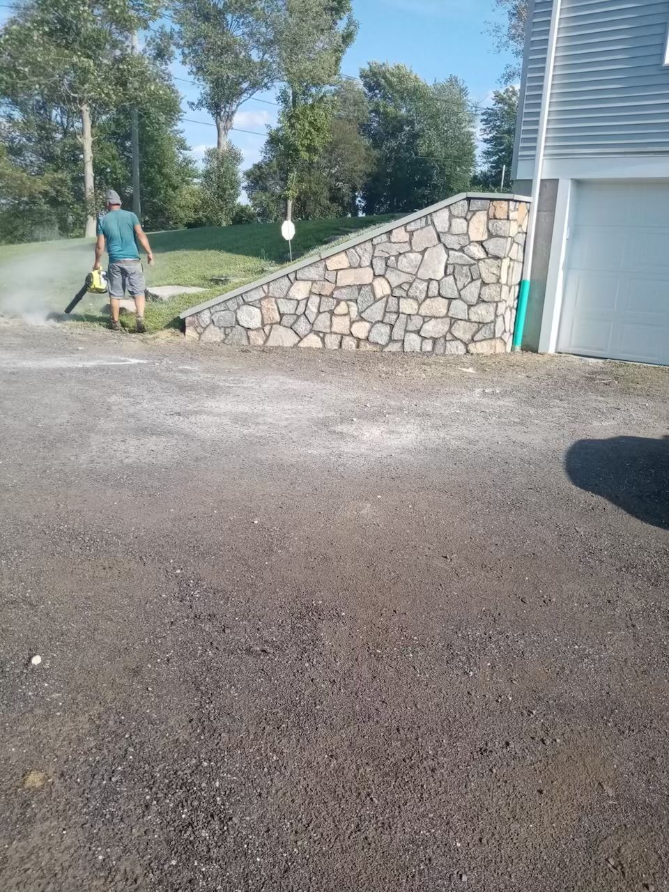 A man is standing in a driveway next to a stone wall.