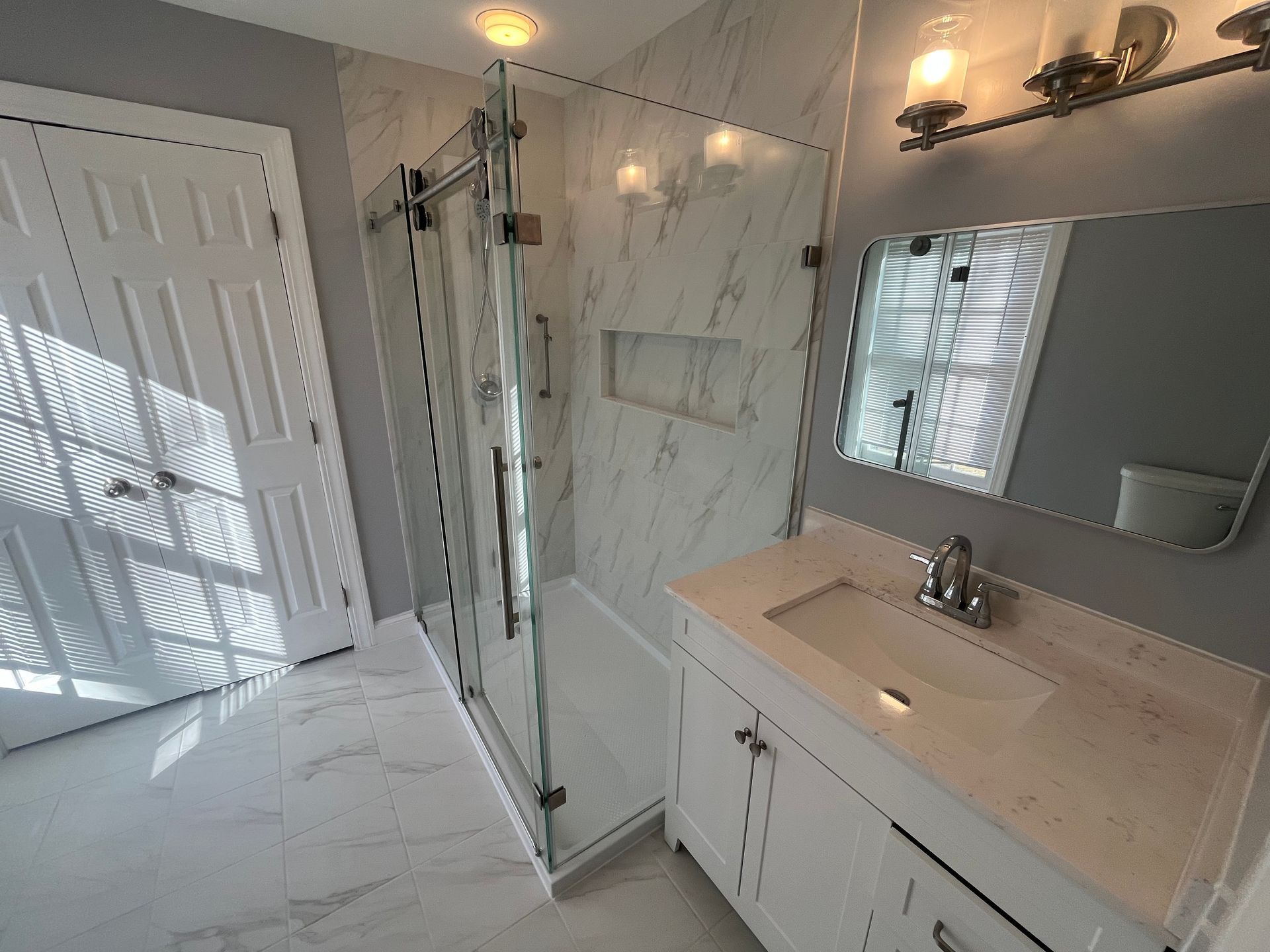 A bathroom with a sink , mirror and walk in shower.