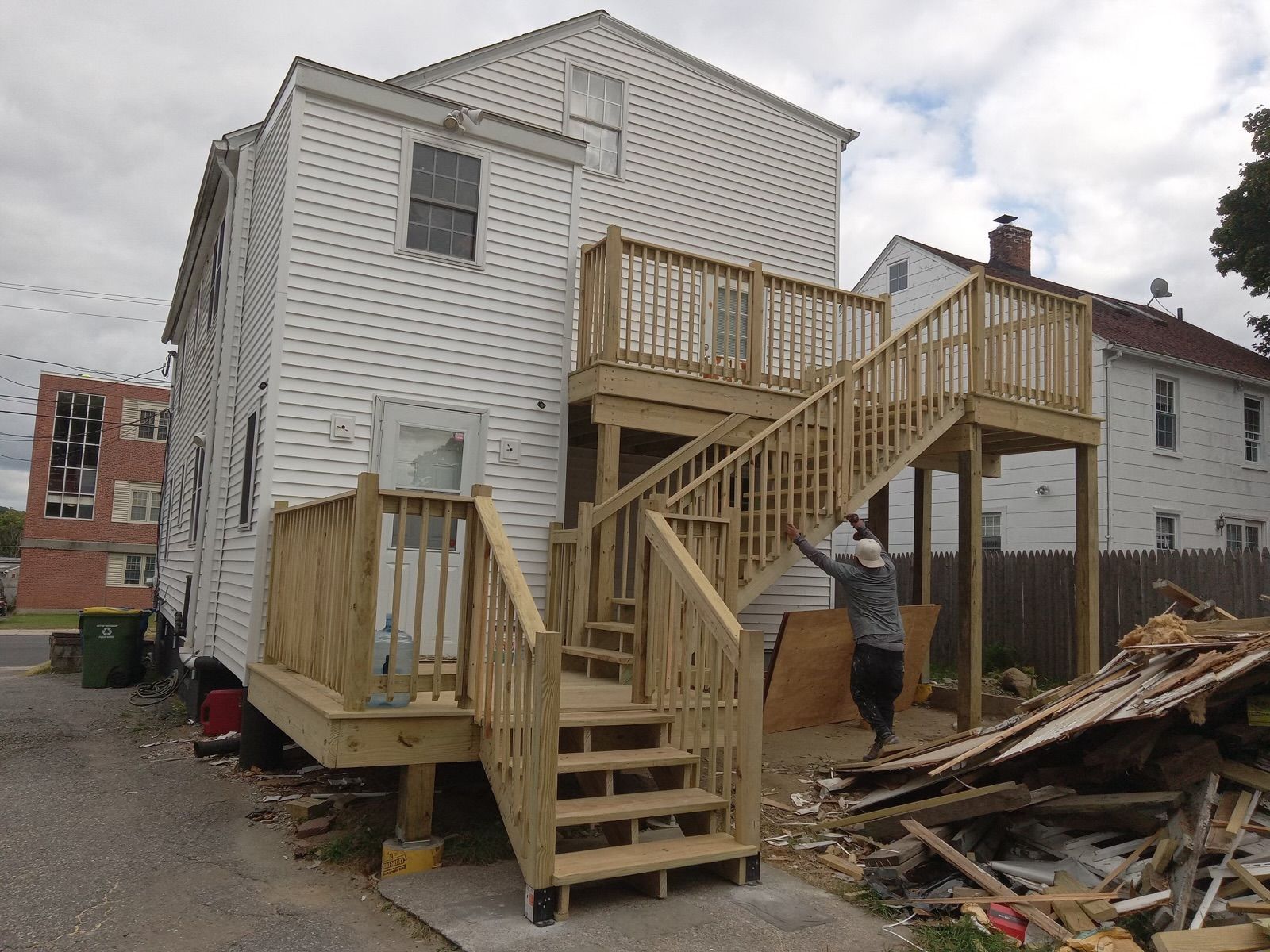 A man is standing in front of a house with a wooden deck and stairs.
