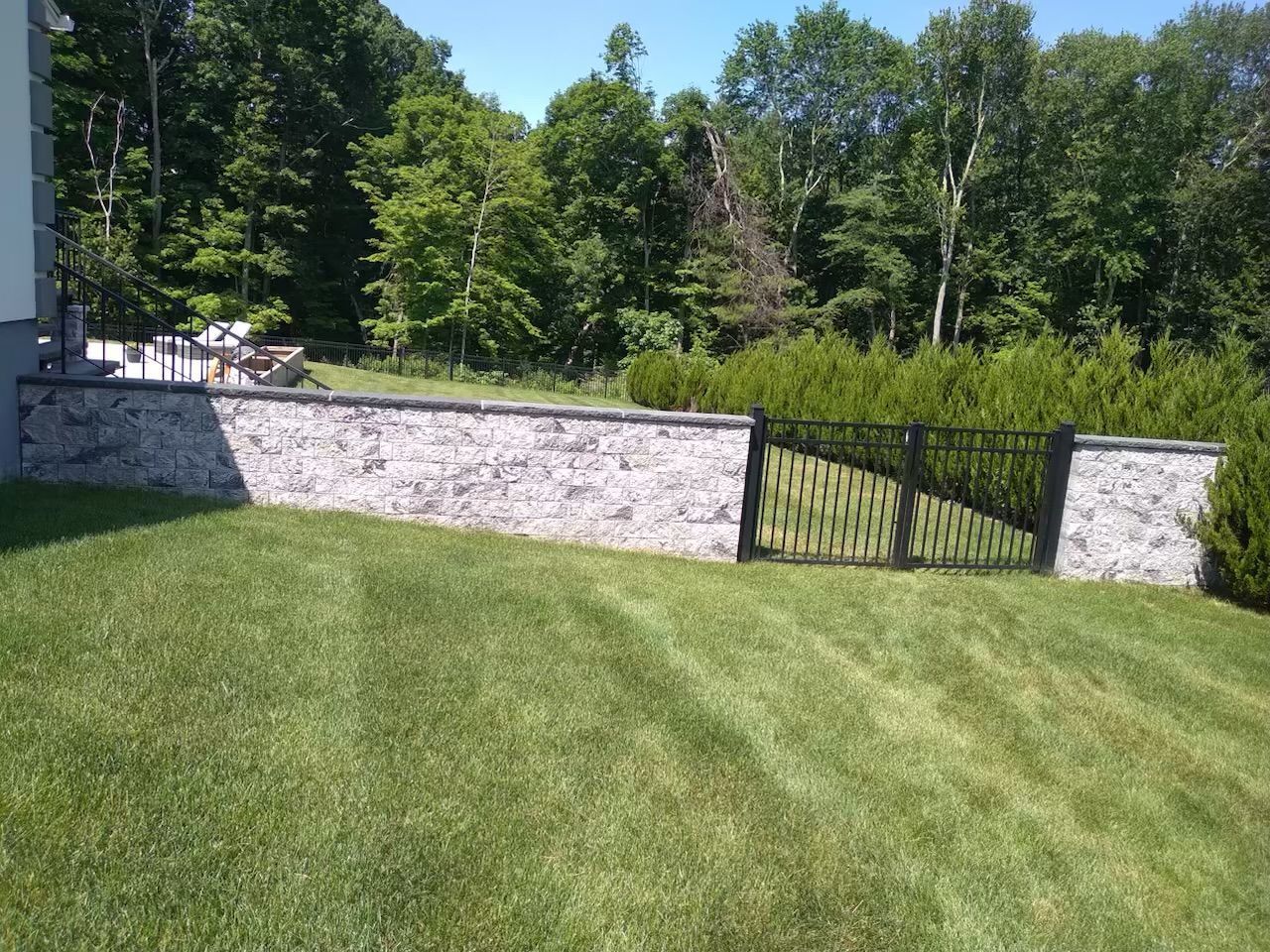 A stone wall surrounds a lush green lawn with trees in the background.