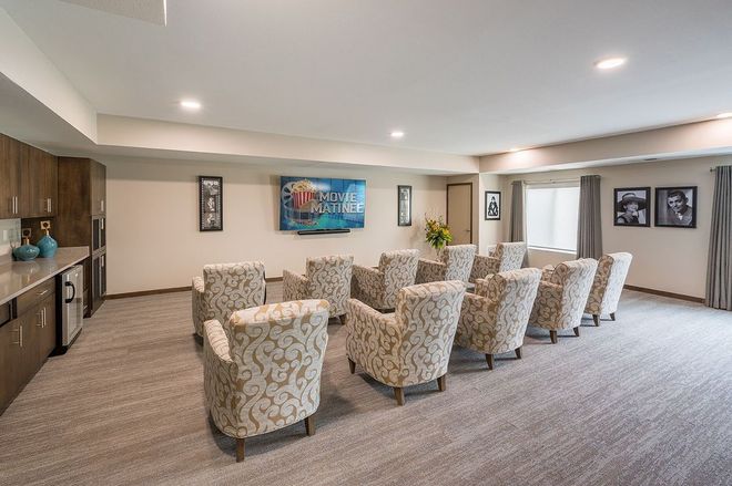 Cozy theater room with patterned armchairs, large TV, and small bar area with granite counter.