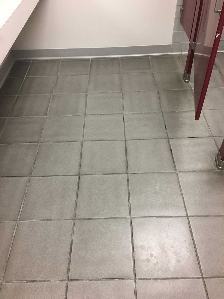 Gray tiled floor in a bathroom with red stall doors, and a white wall.