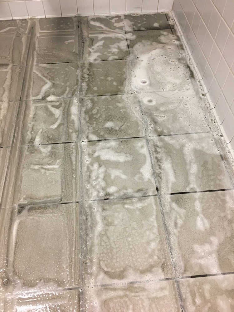 Foamy cleaning solution on grey tiled floor in a shower.