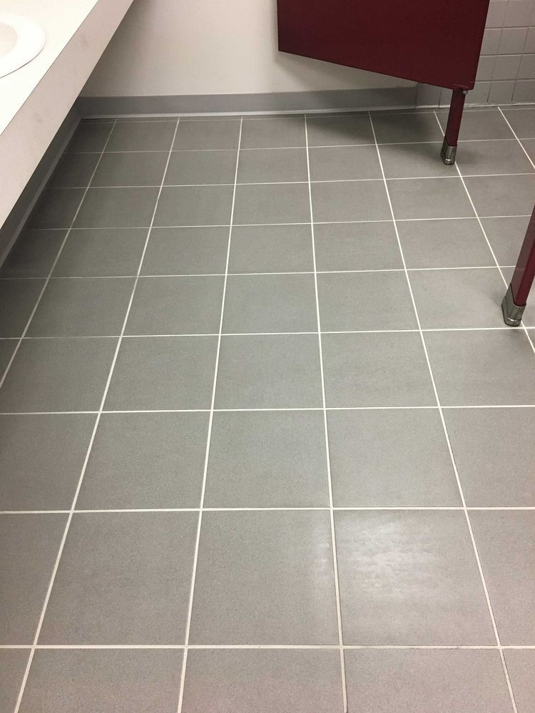 Gray tiled floor in a bathroom with white grout lines. Red cabinet legs are visible.