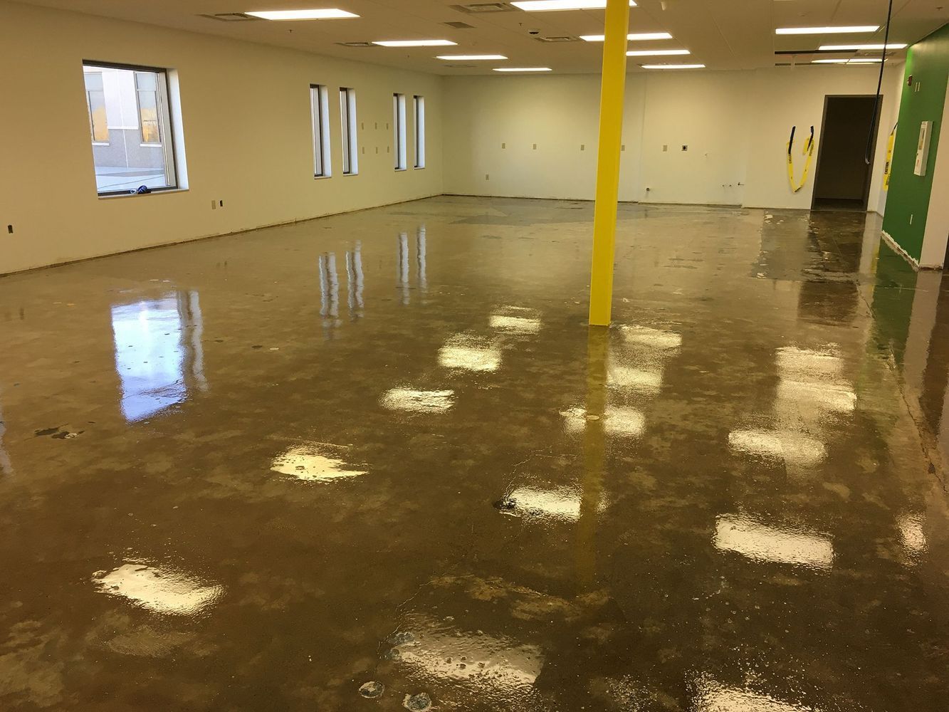 Interior of a room with a reflective, glossy, brown floor; white walls; and yellow support beam.
