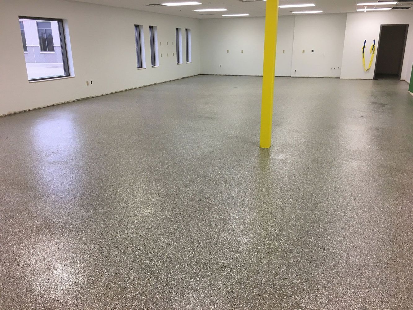 Empty room with epoxy floor, white walls, and a yellow support column.