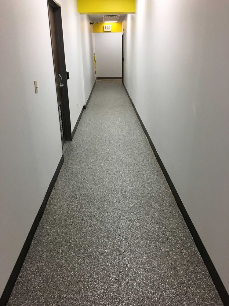 Narrow hallway with white walls, speckled gray floor, and yellow ceiling. Doors on left and ahead.