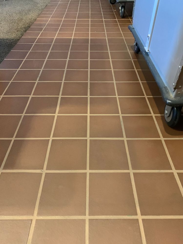 Brown tiled floor with white grout, a cart with wheels is on the right.
