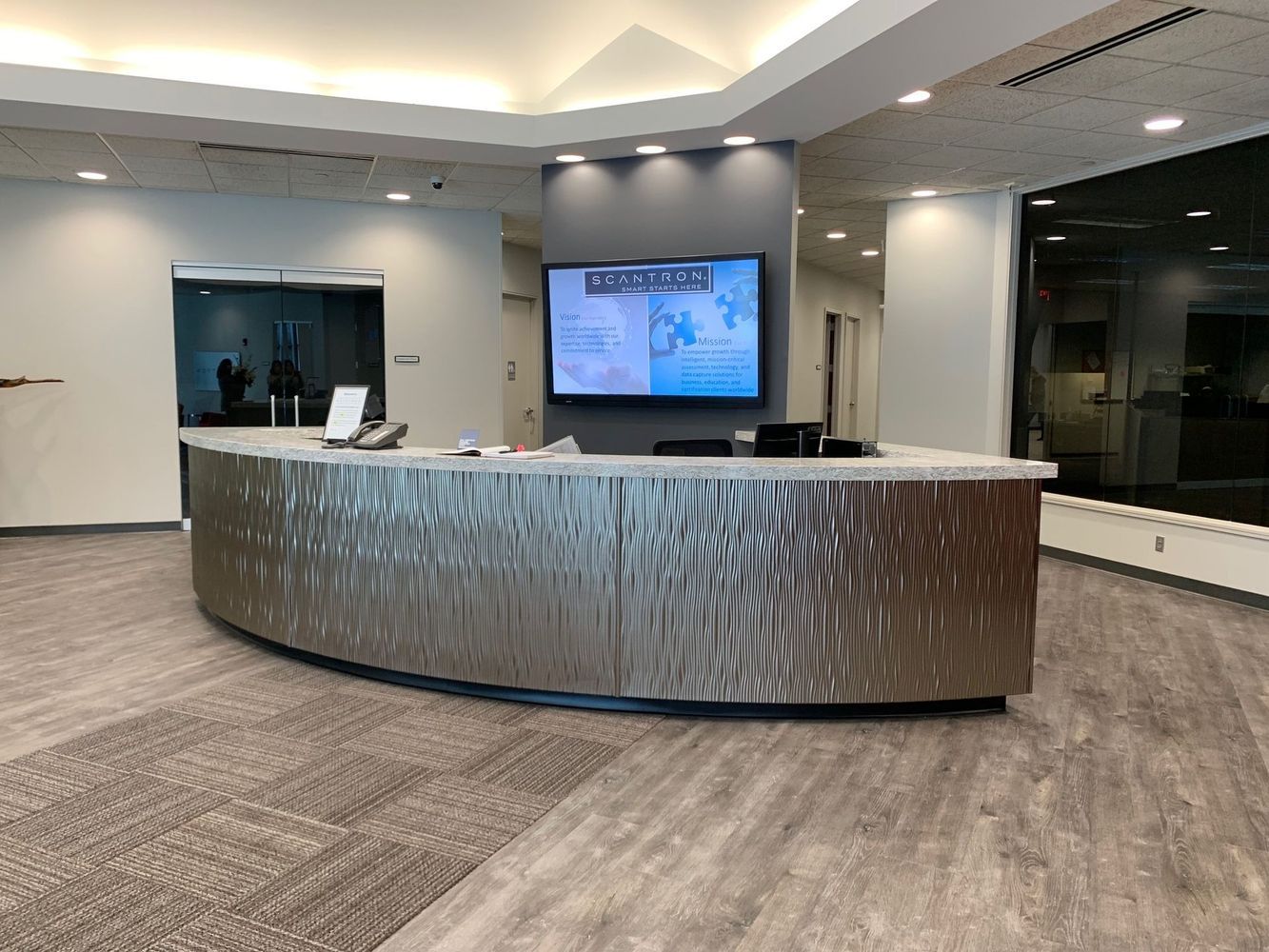Reception desk with metallic textured front, digital display, and light-colored carpet.