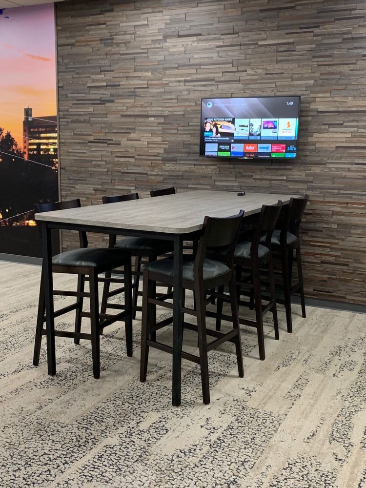 Long table with eight bar stools in front of a stone wall with a mounted TV.