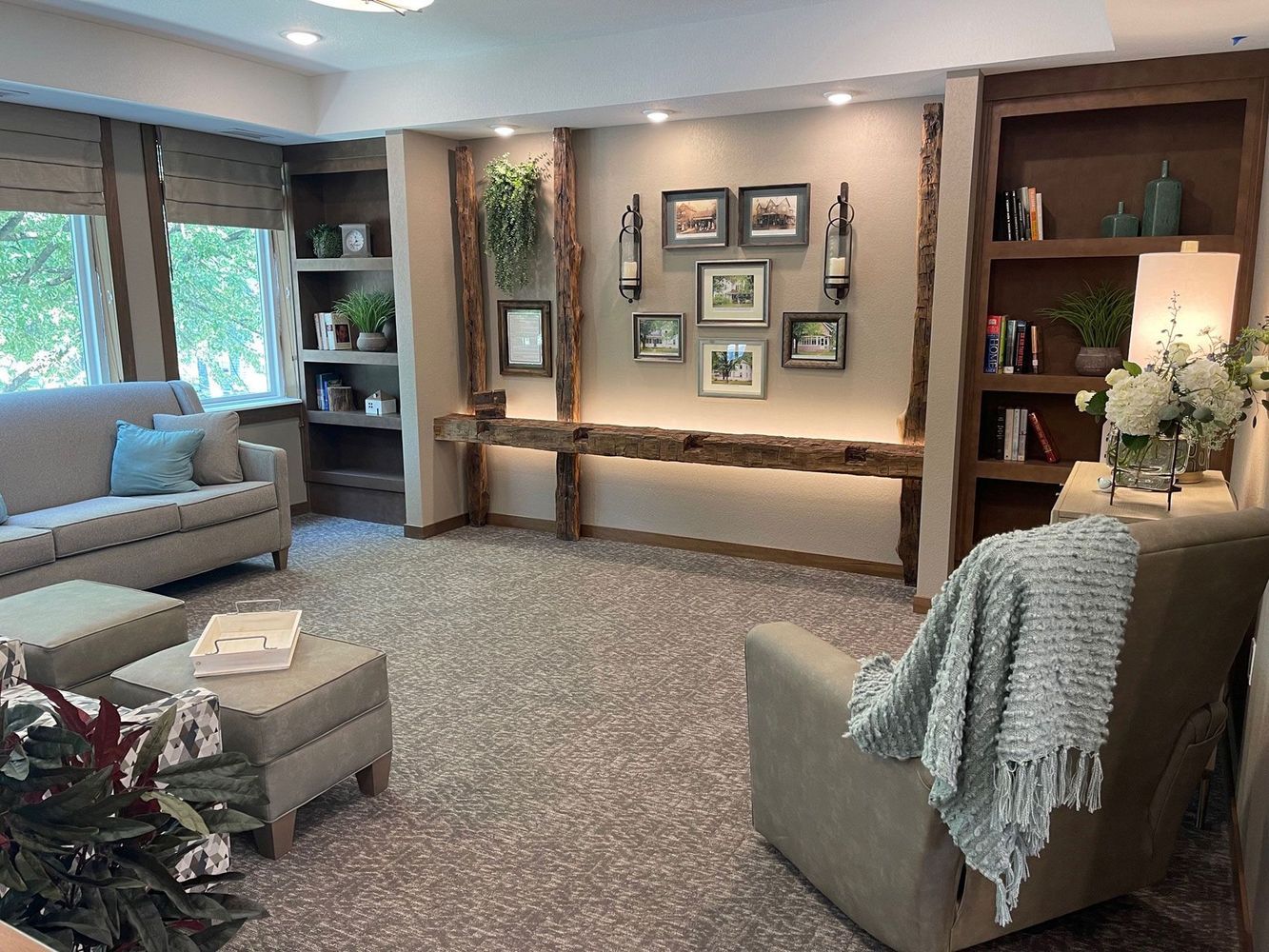 Cozy living room with beige sofa, armchair, and ottoman. Built-in shelves, artwork, and greenery on display.