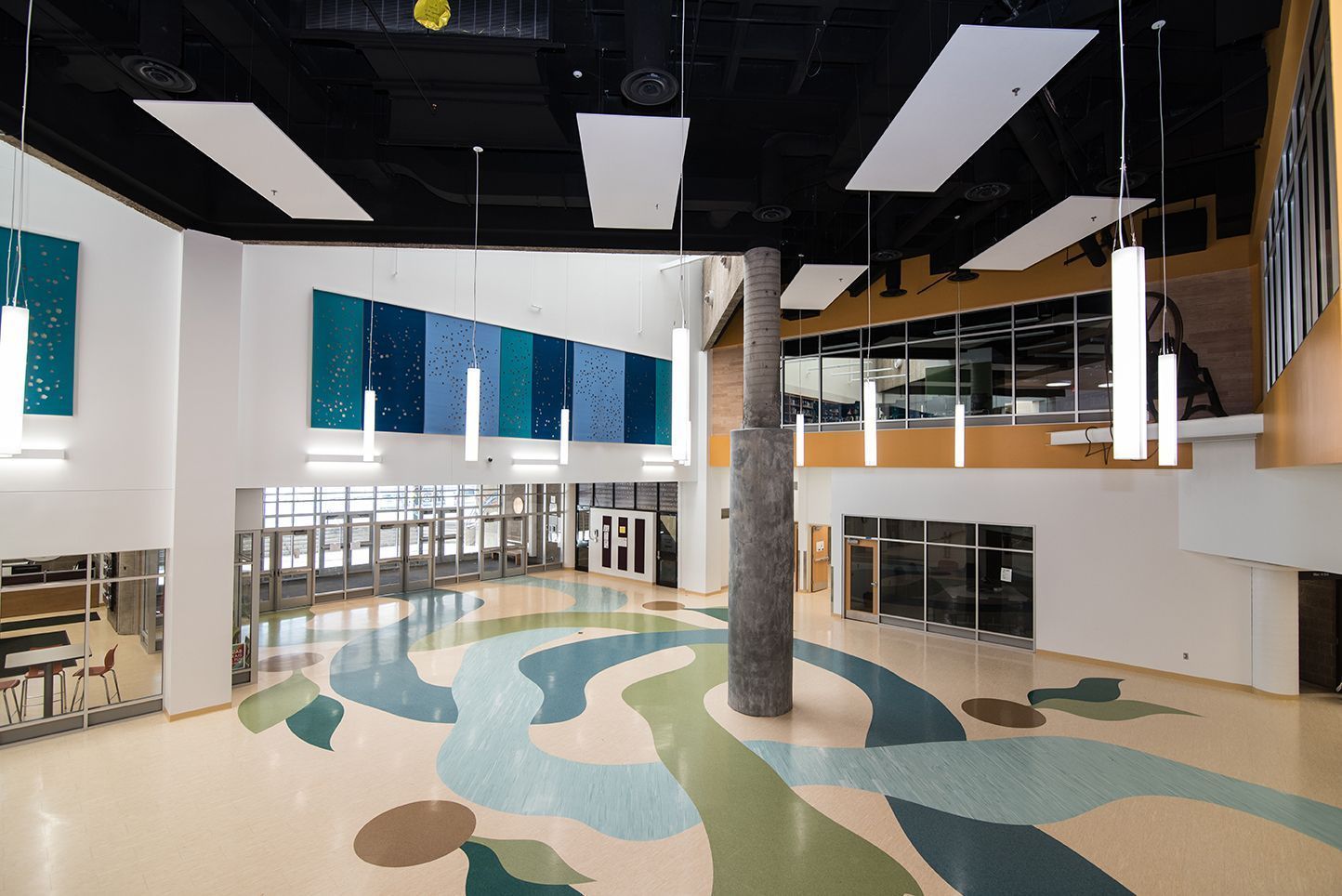 Spacious lobby with colorful floor design, blue and green wall decor, and hanging lights.