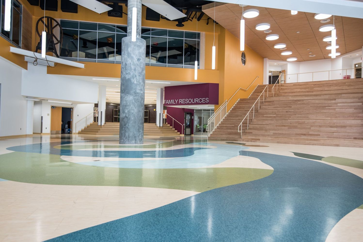 Large school foyer with colorful flooring, central pillar, staircase, and burgundy accent walls.