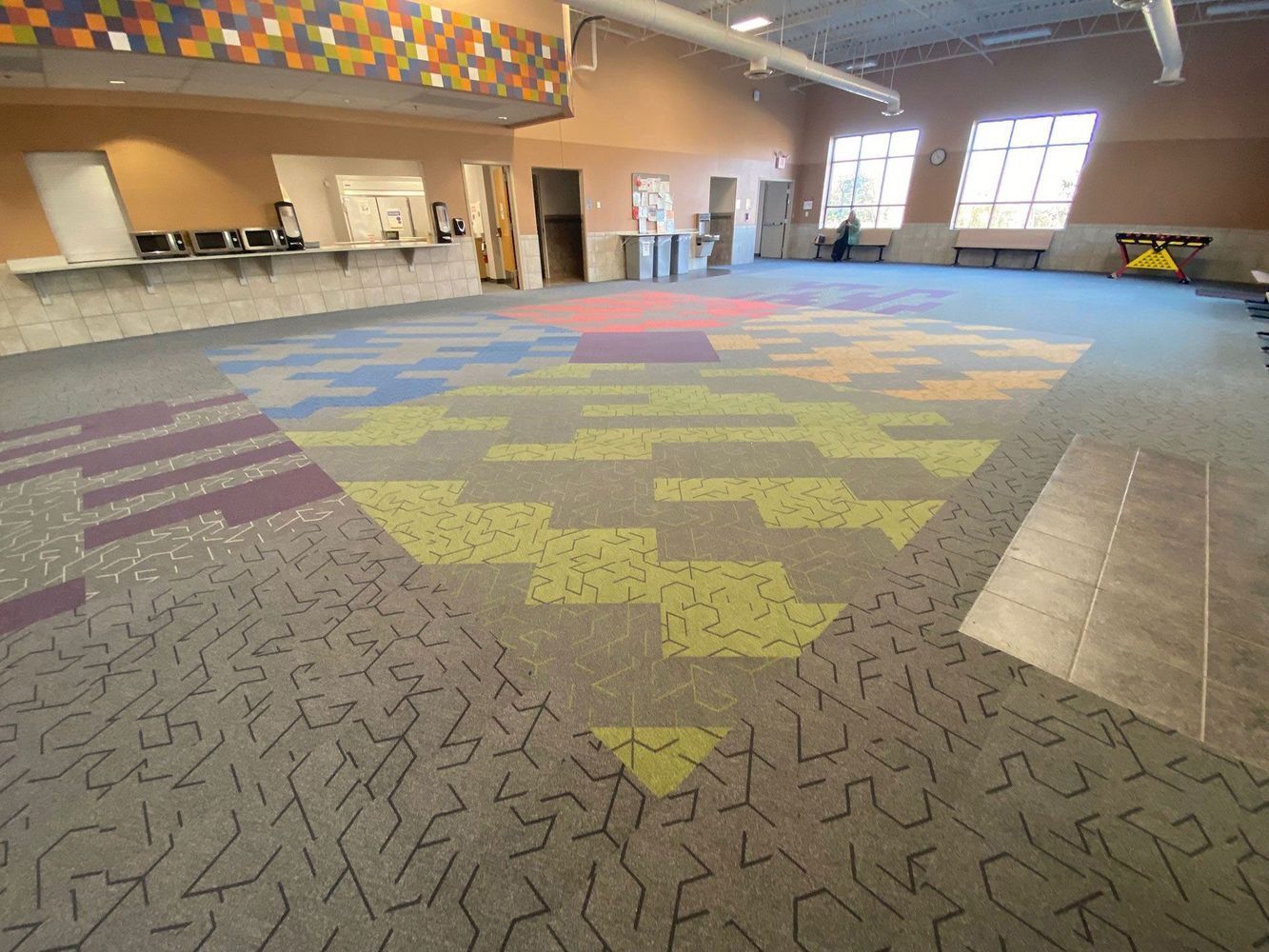 Wide-angle shot of a large open room with colorful geometric carpet and counter/wall art.