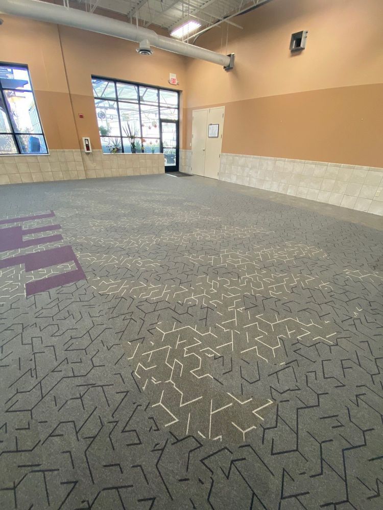 Empty room with patterned gray carpet, tan and purple walls, and large windows.