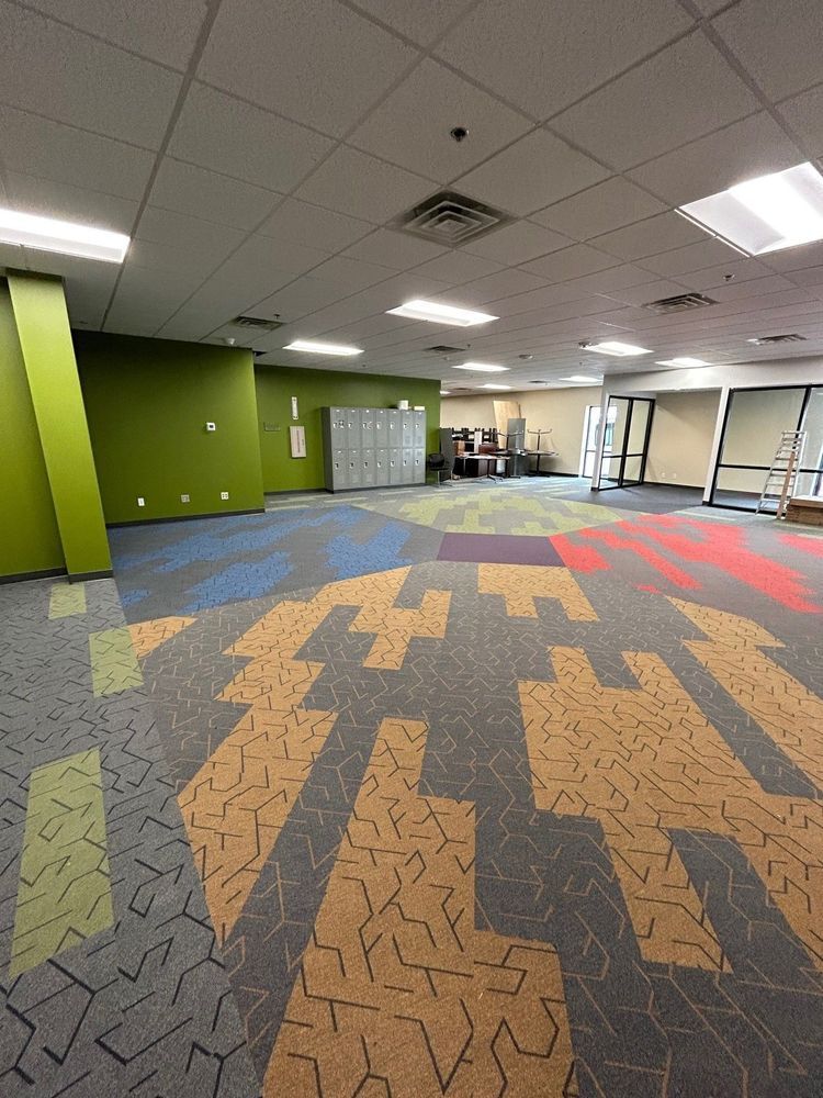 Empty room with colorful patterned carpet and green accent walls. Lockers and windows are visible.