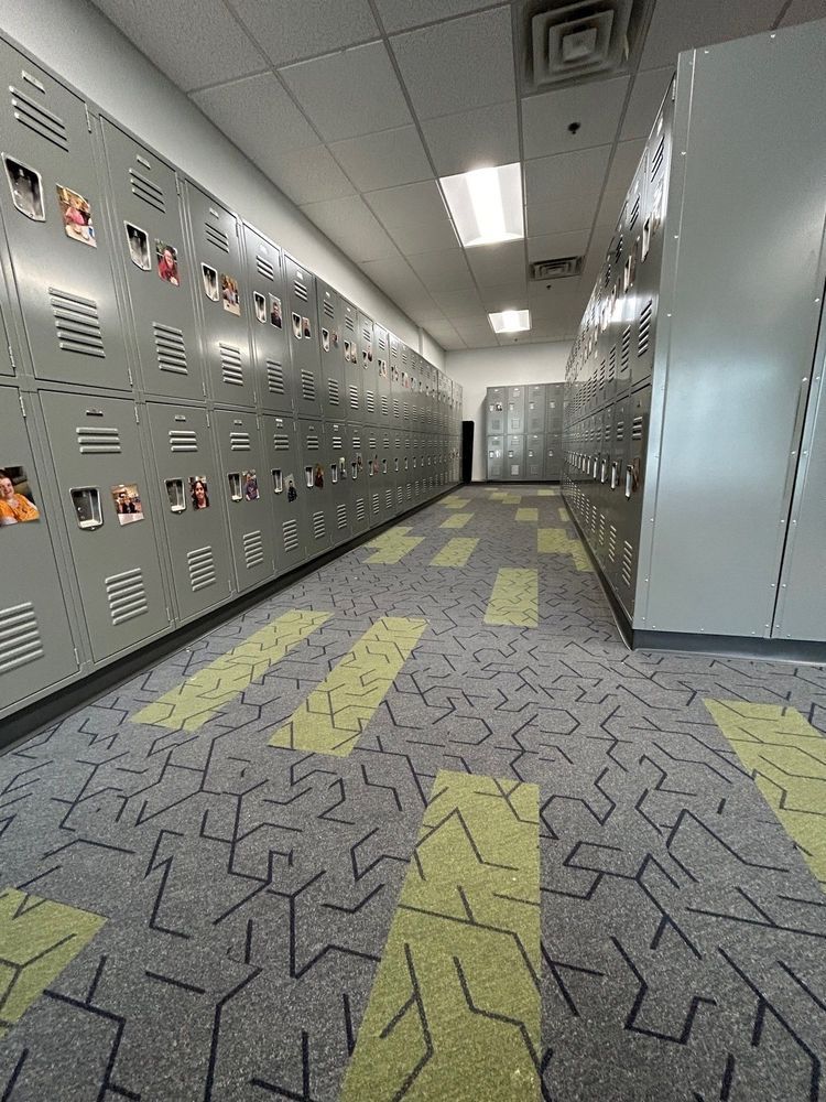 Hallway with rows of gray lockers, patterned carpet, and overhead lighting.