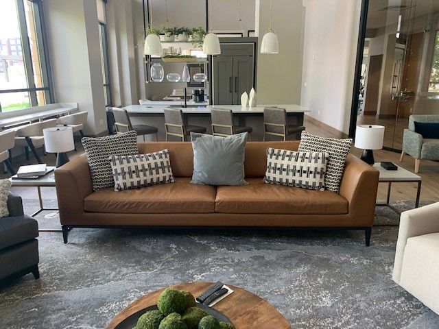Living room with brown leather sofa, pillows, and kitchen in the background.