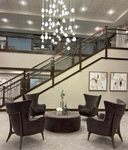 Lobby with stairs, brown chairs, and a round ottoman. Modern light fixture hangs overhead. Two paintings on the wall.