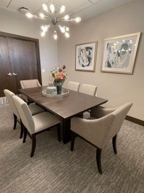 A dining room with a wooden table, six chairs, artwork, and a chandelier.