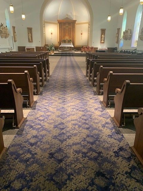 Church interior with pews, a patterned blue and gold carpet aisle, and a wooden altar.
