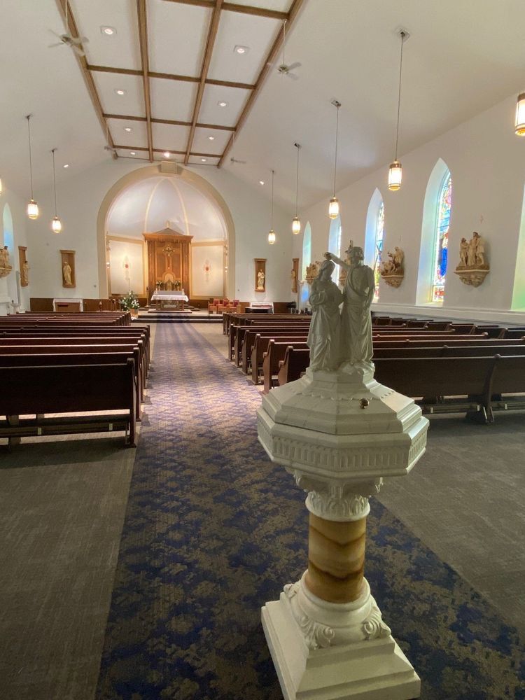 Interior of a church: Rows of pews, altar at end. Baptismal font in foreground.
