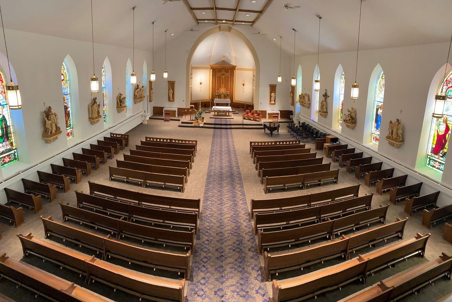 Interior view of a church with rows of wooden pews, stained glass windows, and a central altar.