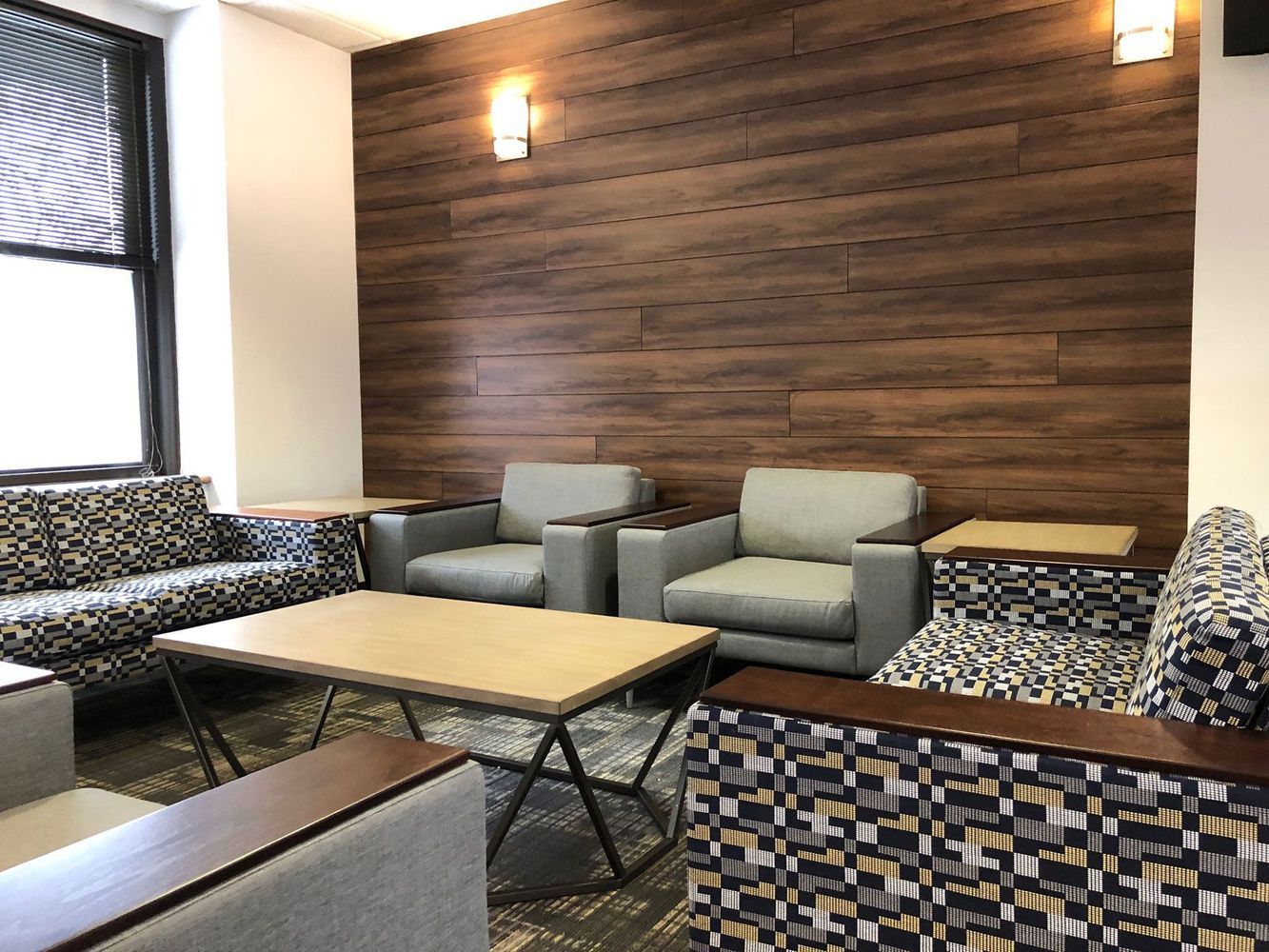 Lounge area with gray armchairs, patterned sofas, and a wood-paneled wall.