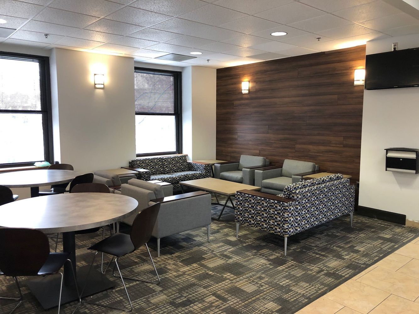 Lounge with seating, round tables, and a wood-paneled wall.