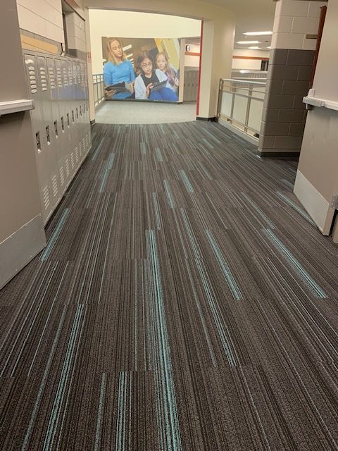 Hallway with gray and teal patterned carpet, lockers on the left, poster at the end.