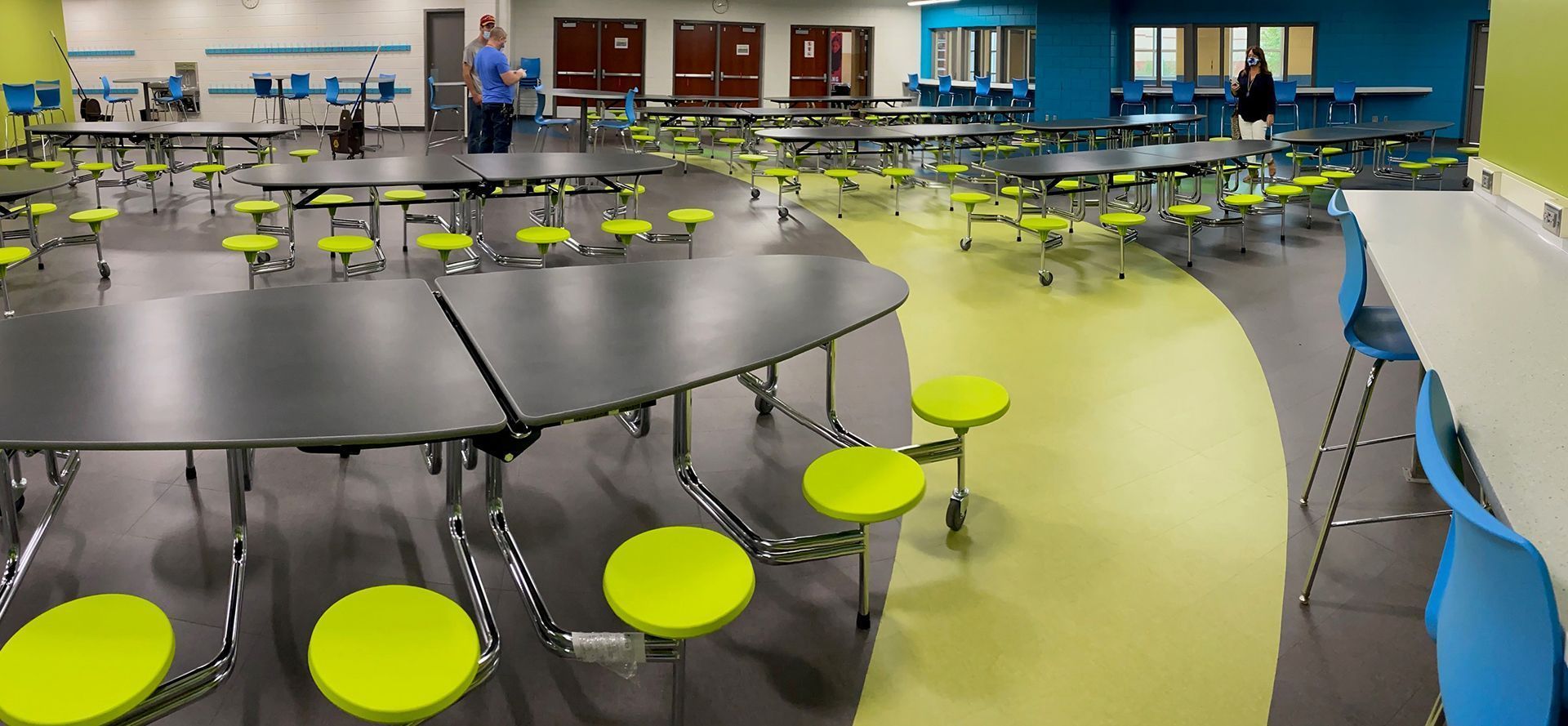 A cafeteria with tables, lime green stools, and people walking.