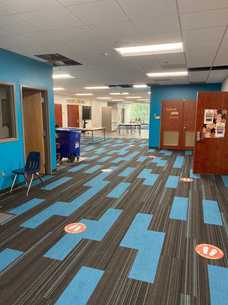 Hallway with blue and black carpet, blue walls, wooden doors, and social distancing markers.