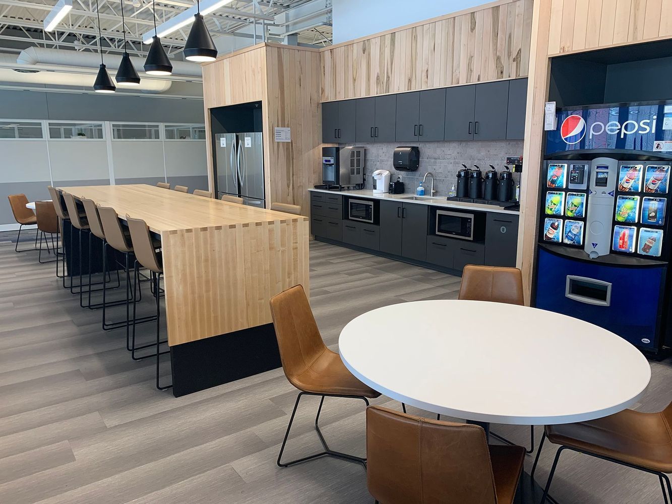 Office breakroom with a large counter, tables, chairs, cabinets, and a soda machine.