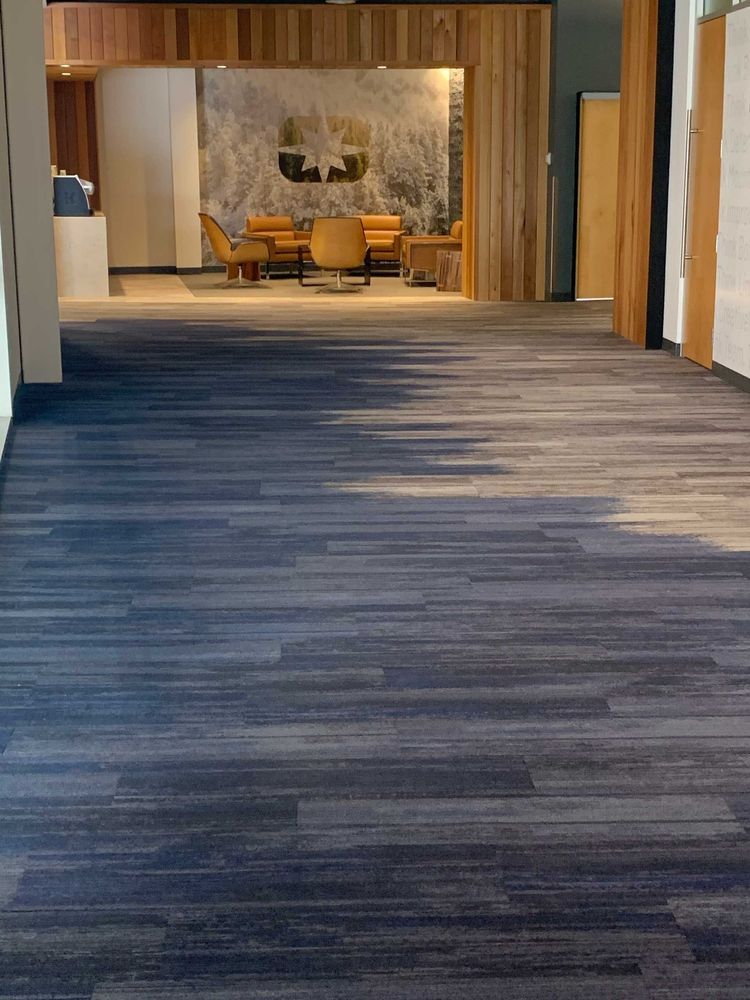 Blue and gray patterned floor in an office hallway leading to a seating area with wood accents and artwork.