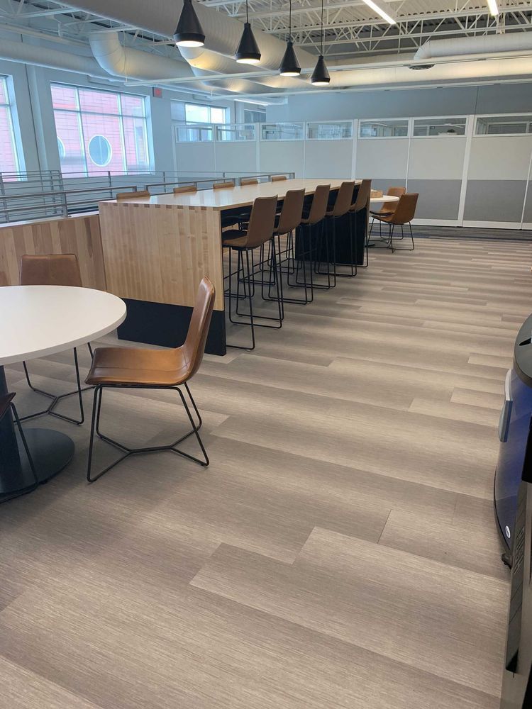 Interior view of a modern lounge area. Long wooden table with bar stools, round table with chairs, and neutral-colored flooring.
