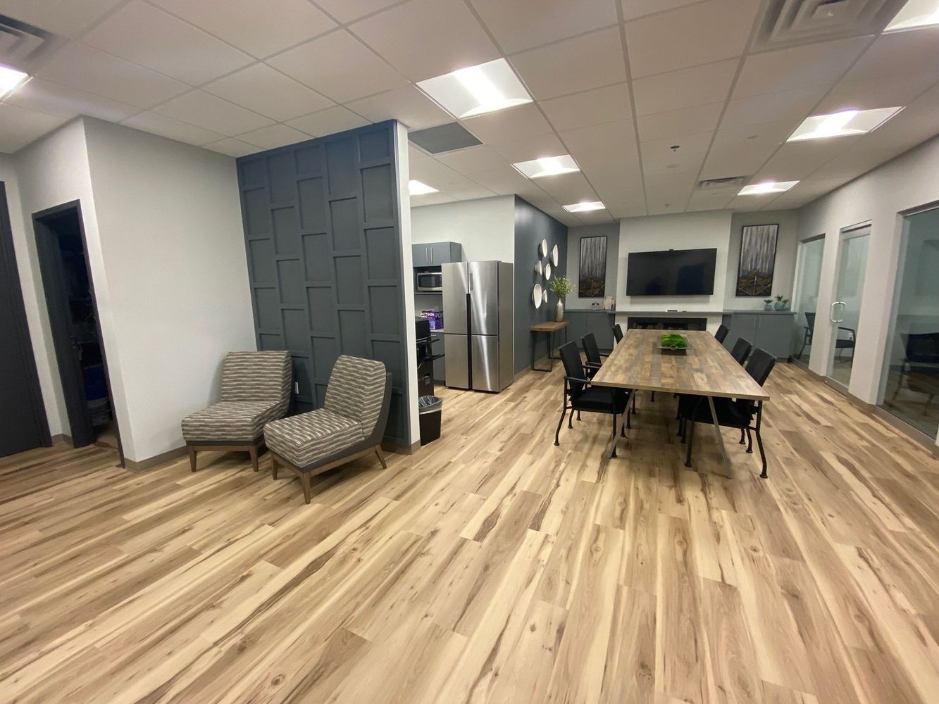 Office interior with wood floors, waiting area with chairs, conference table, and a stainless steel refrigerator.