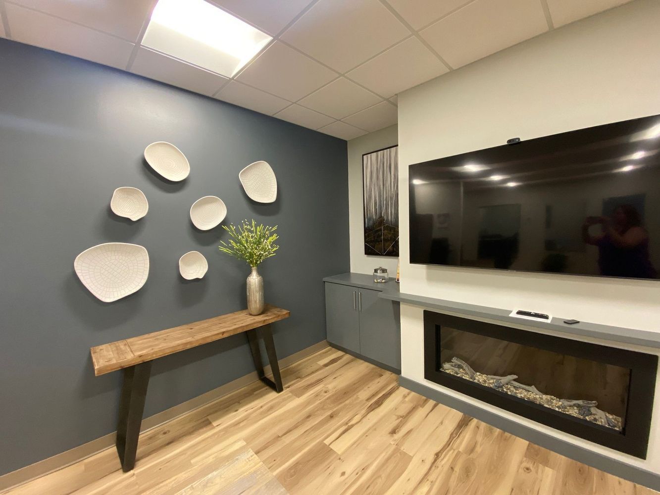 Cozy waiting room with fireplace, TV, wood floor, decorative wall art and small bar.