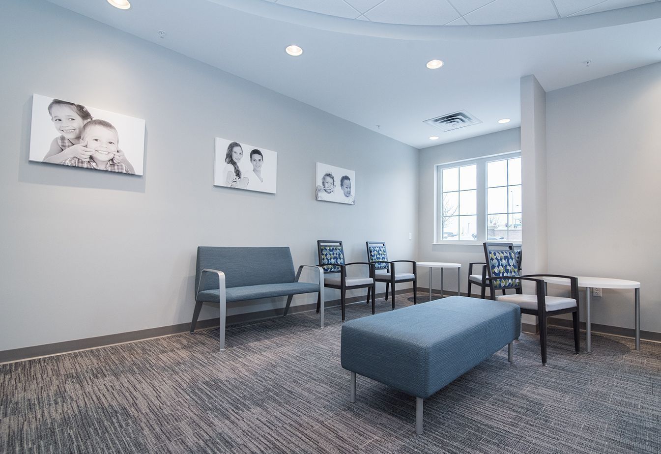 Waiting room with gray walls, seating, photos, and a window.