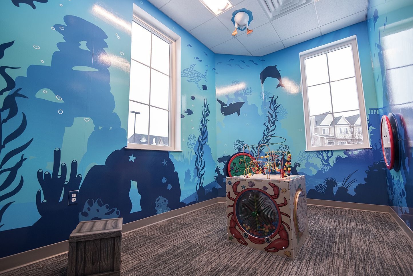 Underwater-themed room with blue murals, windows, and toy-covered crate.