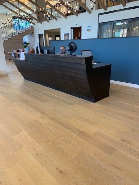 Dark wood reception desk in open room with wood floor and a person sitting behind it.