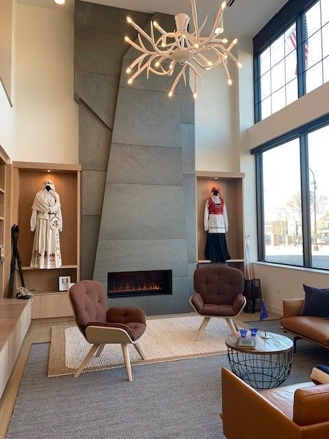 Modern interior with a large fireplace, armchairs, and display niches with clothing. Bright, airy space with large windows.