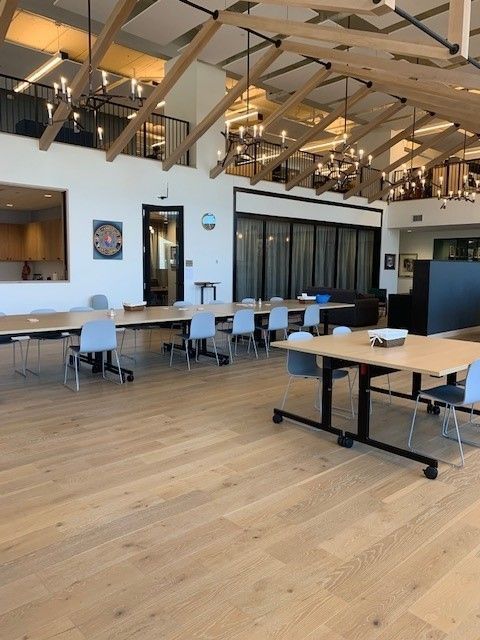 A bright, spacious room with tables and chairs, wood floors, and chandeliers.