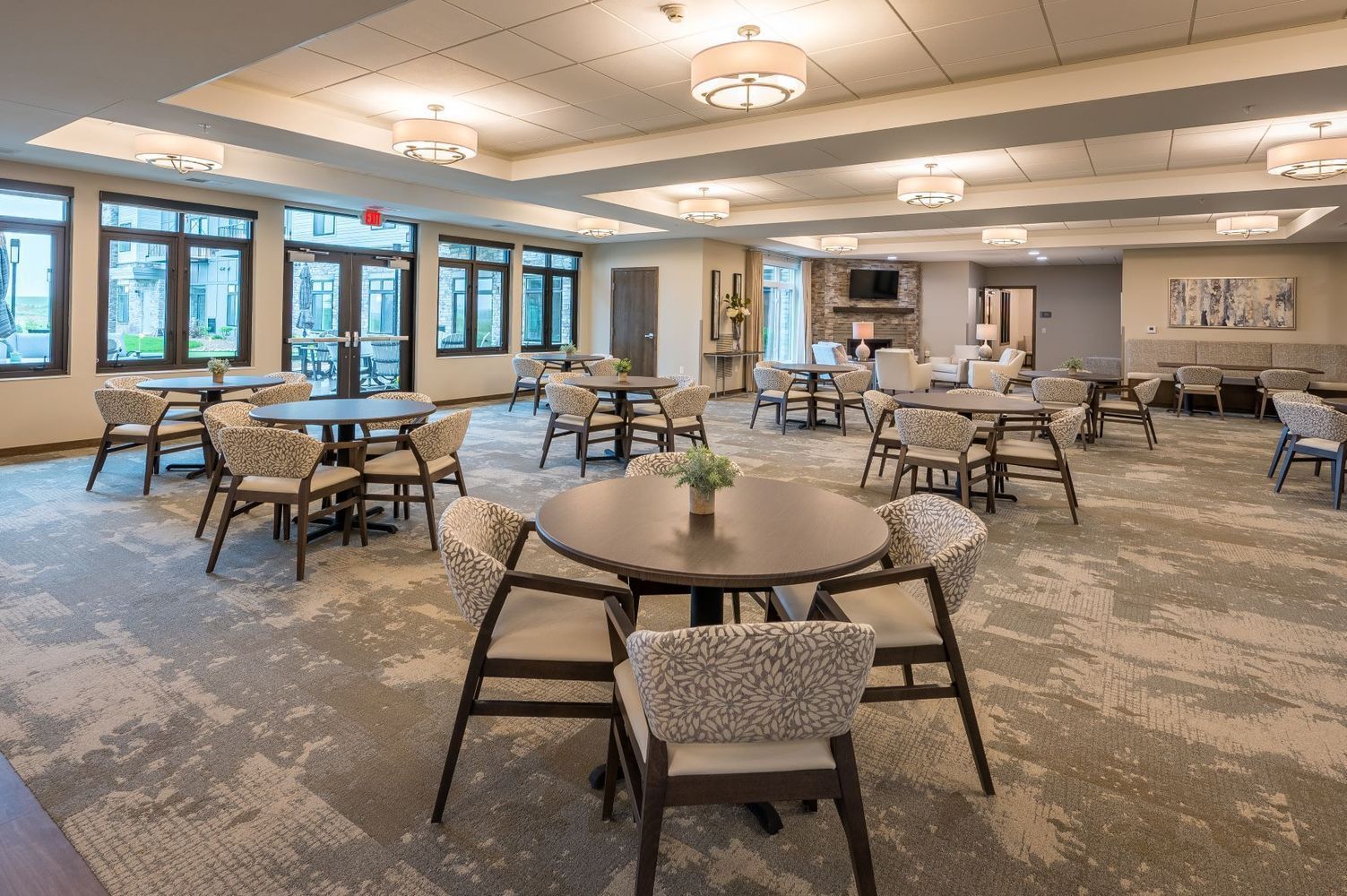 Dining area with round tables, chairs, and large windows. Beige and gray color scheme.