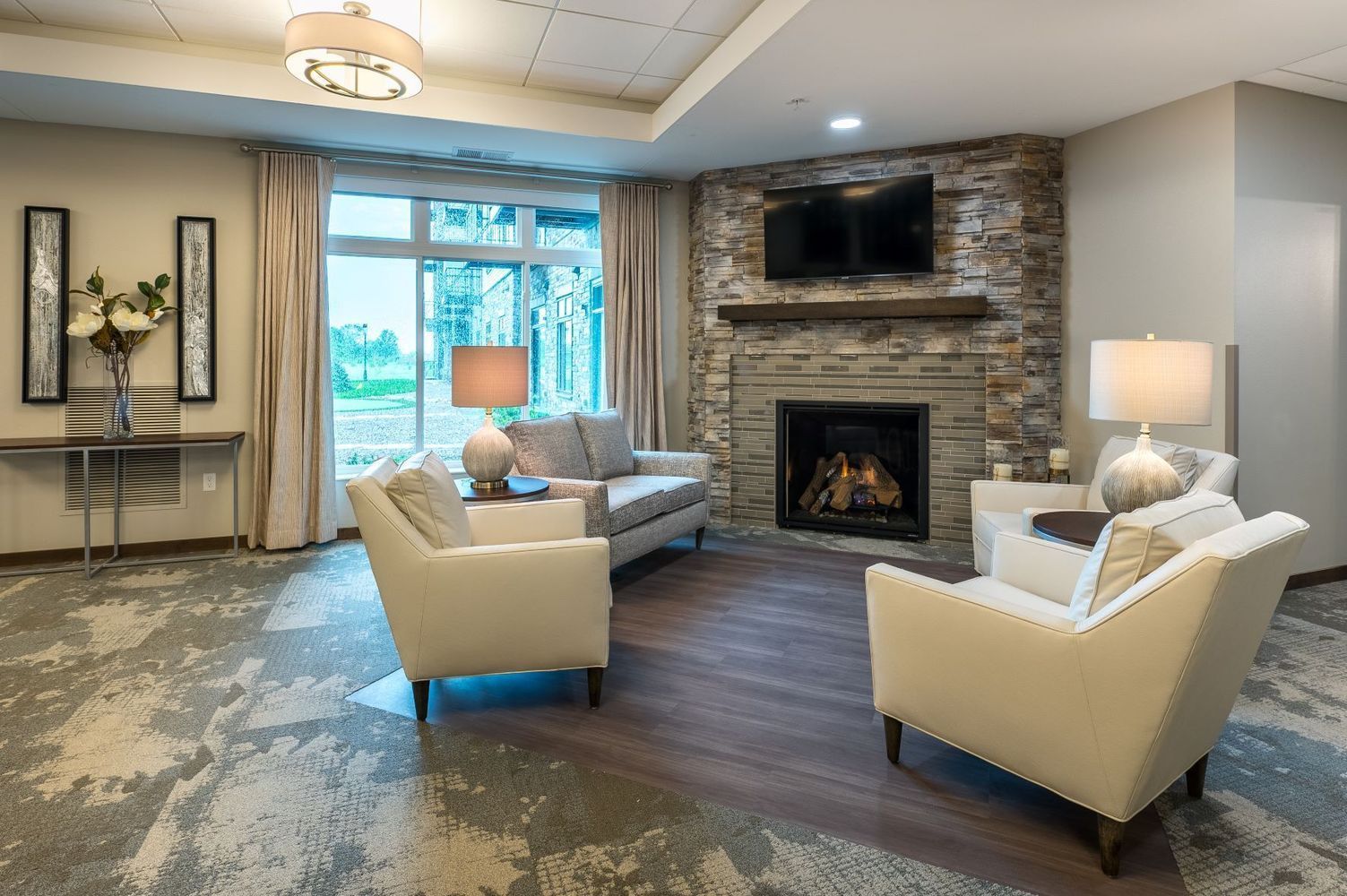Cozy living room with fireplace, seating, and large window. Neutral tones with wood and stone accents.