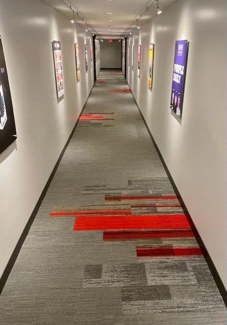 Long hallway with gray carpet, red accents, and framed posters on the walls.